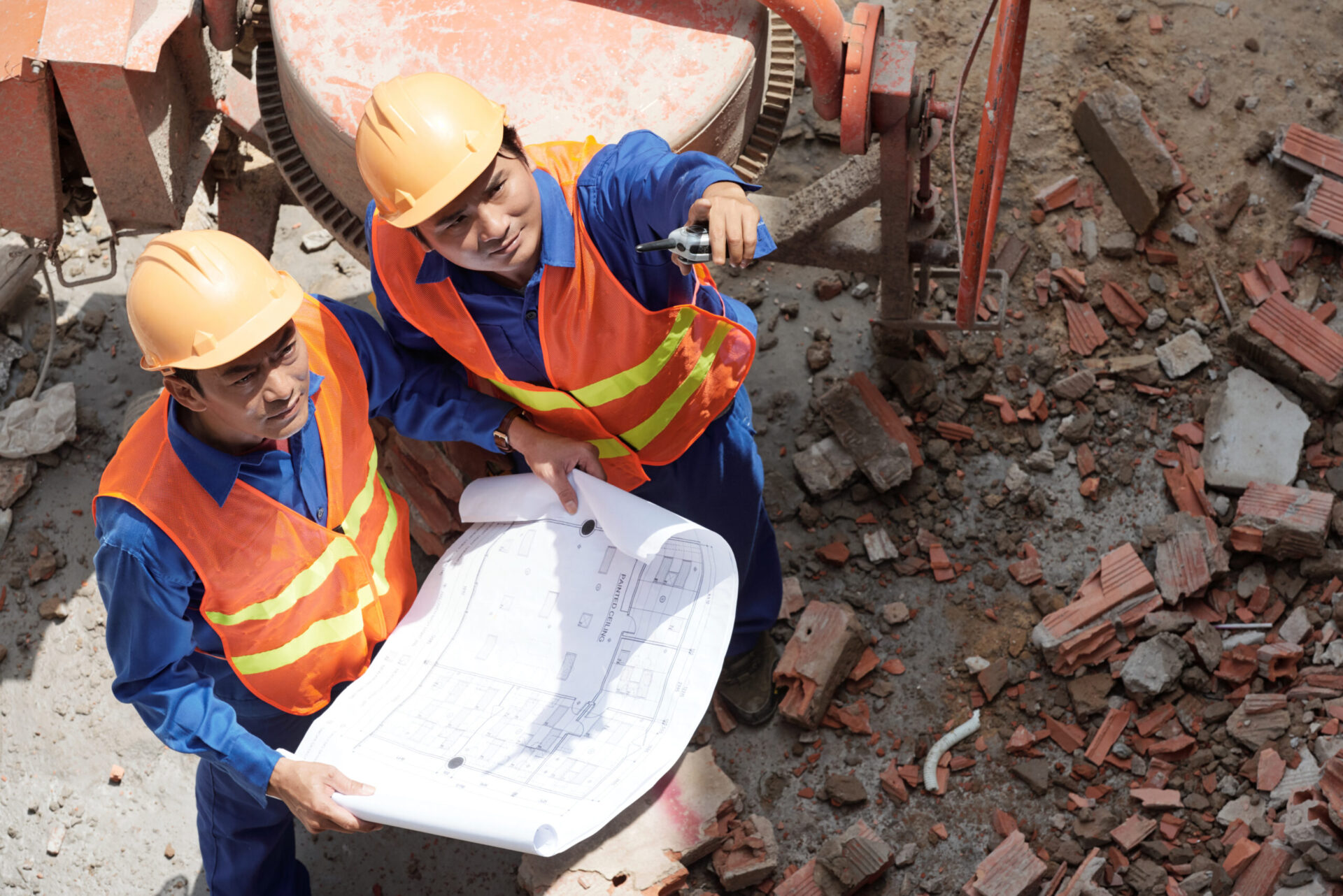 Serious Asian contractors with blueprint inspecting building under construction