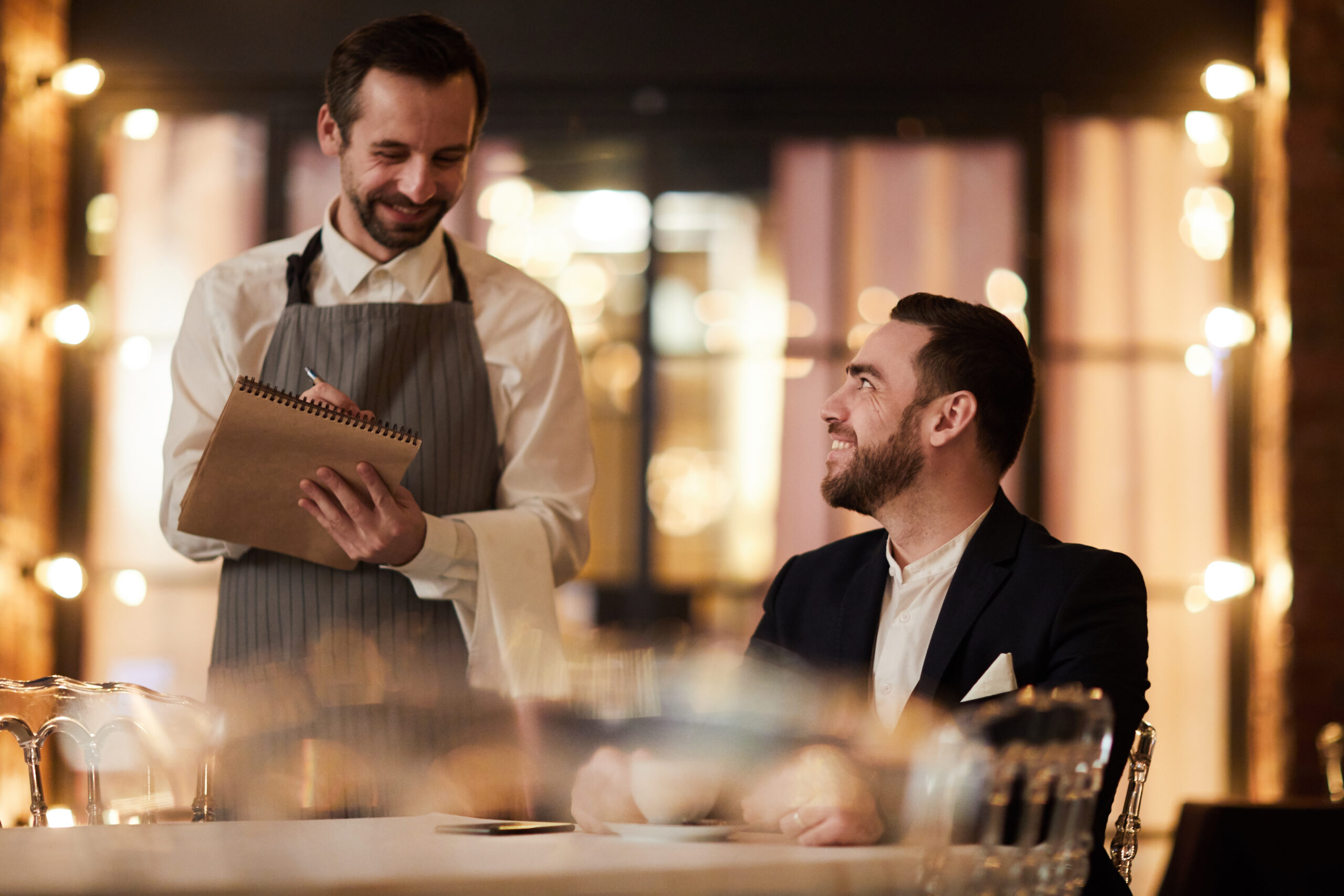 Portrait of smiling businessman ordering food in luxury restaurant with waiter standing at table, copy space