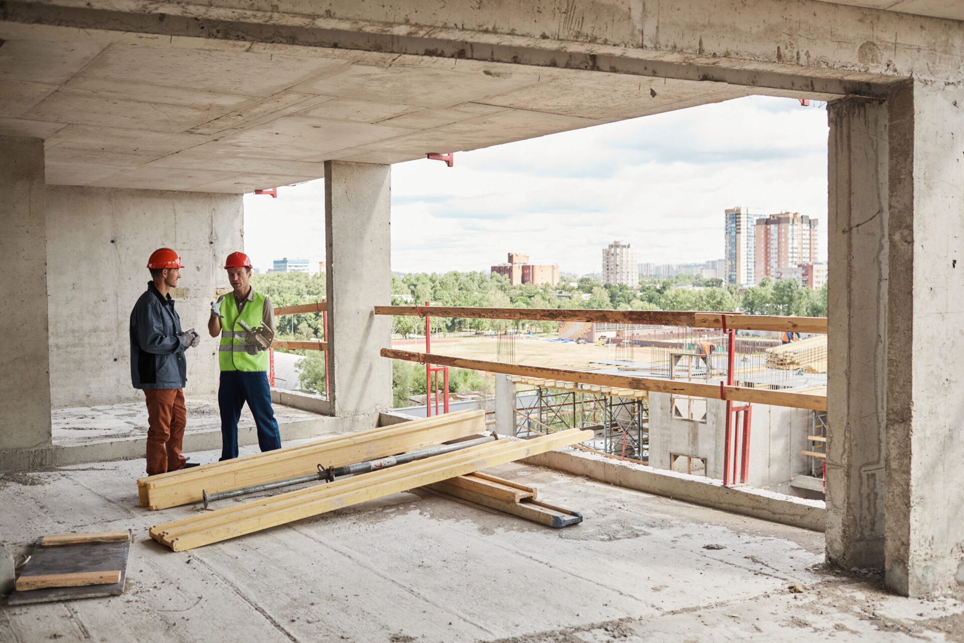 Wide angle view at two construction workers wearing hardhats while standing at construction site, copy space